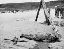 (details) A dead GI in front of a "rape" obstacle.In the background of hedgehogs and a half track.