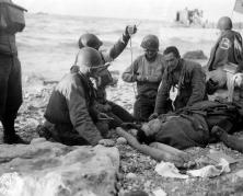 (détails) Des soldats apportent une première aide aux survivants d'une barge de débarquement coulée, le "Jour-J", 6 Juin 1944. En second plan les LCT 29 et 30 A l'horizon
