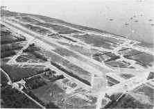 (détails) Vue d'ensemble de l'aérodrome de St-Pierre-du-Mont. Au fond à gauche la Pinte du Hoc. Au large des navires au mouilage, extension de la rade 'Omaha Beach. Au pr